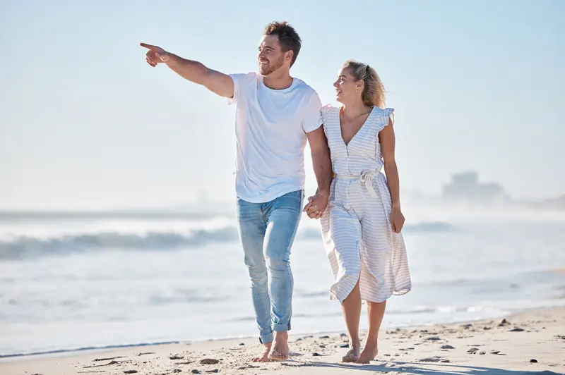 Ein Paar spaziert am Strand, der Mann zeigt in die Ferne, symbolisiert das Anwenden praktischer Tipps zur Rückeroberung des Ex.
