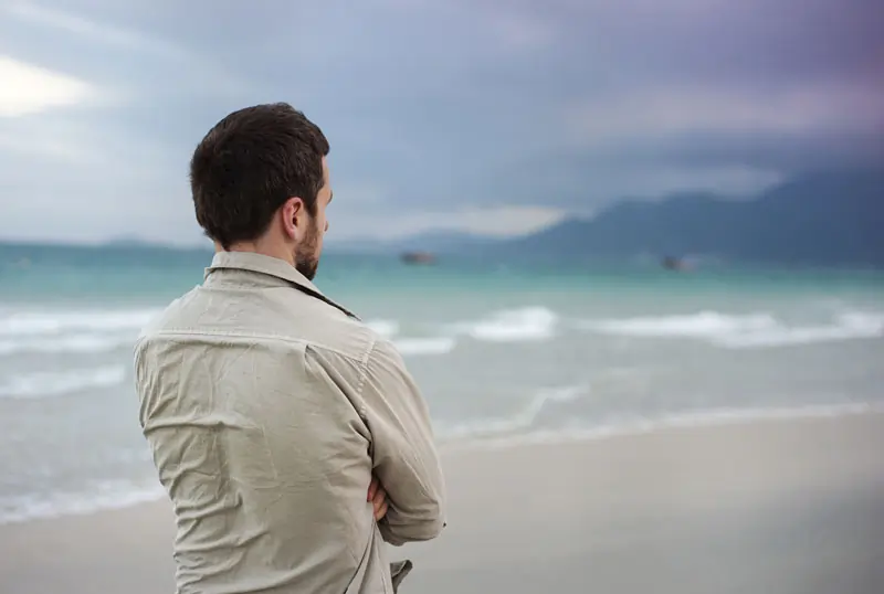 Eine Person steht nachdenklich am Strand und blickt auf das Meer, symbolisiert den Umgang mit Liebeskummer und psychologische Reflexion.