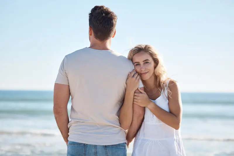 Ein lächelndes Paar am Strand, die Frau hält den Arm des Mannes, symbolisiert Hoffnung und die Möglichkeit, den Ex zurückzugewinnen.