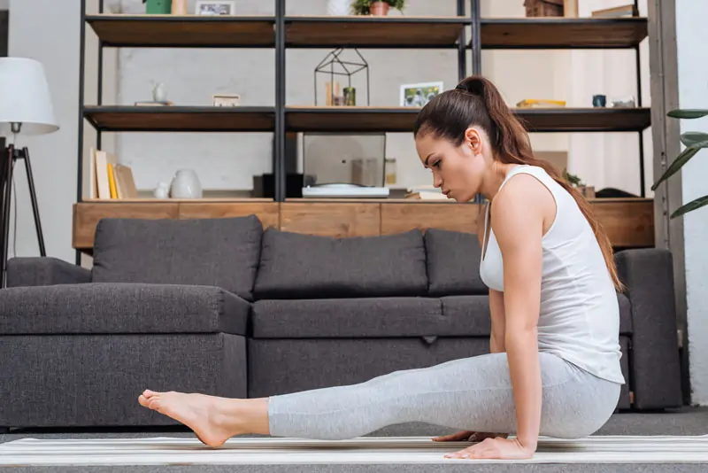 Eine Frau praktiziert Yoga im Wohnzimmer, um Selbstfürsorge und innere Ruhe als Strategien zur emotionalen Bewältigung zu zeigen.