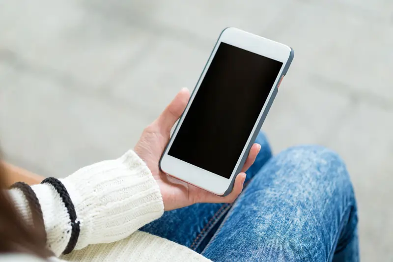 Frau hält Smartphone mit leerem Bildschirm – Zeichen für mangelnden Kontakt und Interesse.
