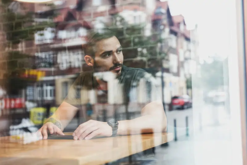 Mann sitzt nachdenklich in einem Café und schaut aus dem Fenster, verdeutlicht Unsicherheit und innere Konflikte, die zu widersprüchlichem Verhalten führen können.